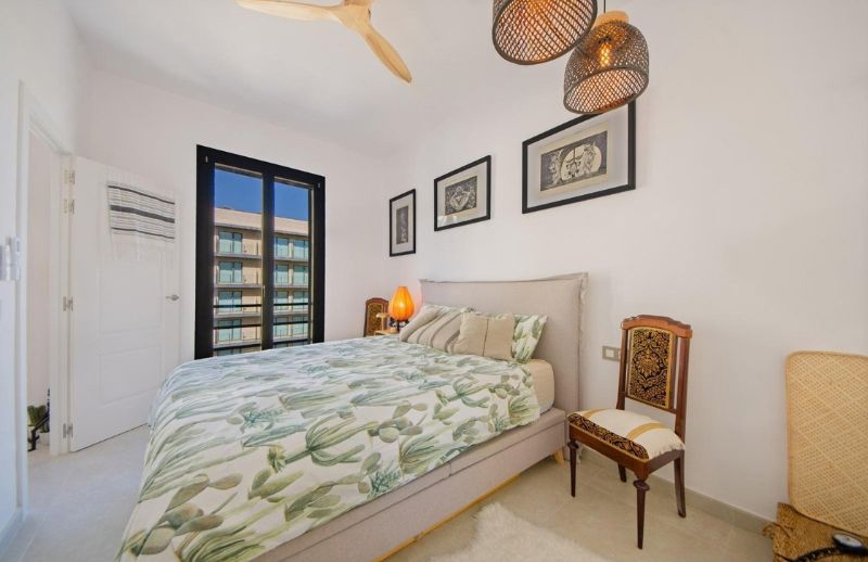Light double bedroom renovation with cactus bedding, wooden ceiling fan, and black window frame in Palma